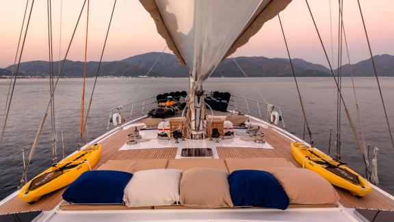 Entspannungsbereich auf dem Vorderdeck mit Kissen und Kajaks auf der Yacht Ubi Bene bei Sonnenuntergang.