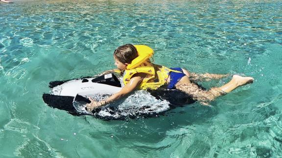 Ein Kind genießt die Fahrt mit einem Seabob im kristallklaren, türkisfarbenen Wasser, ausgestattet mit einer Schwimmwest