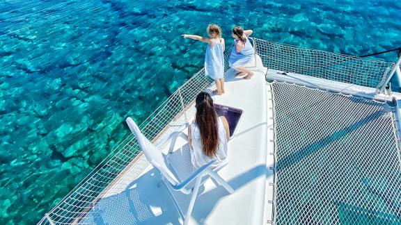 Eine Familie genießt die Aussicht auf das kristallklare Wasser vom Trampolin des Katamarans Marla Lagoon 450F.