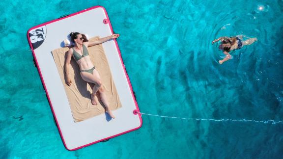 A woman relaxes on a floating mat while a child swims in the crystal-clear water.