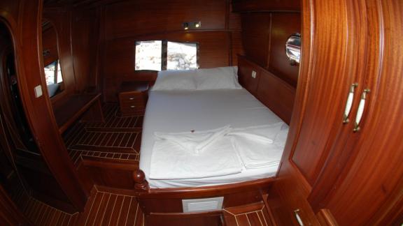 Eine gemütliche Kabine auf der Gulet Sahinoğlu, ausgestattet mit einem komfortablen Doppelbett, Holzmöbeln und Fenstern 