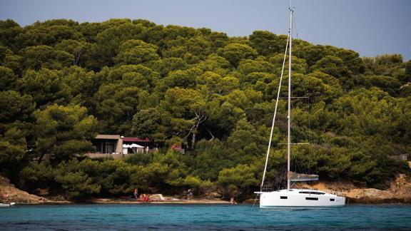 Segelyacht Sirius II liegt vor Anker in ruhigem Wasser an einem bewaldeten Ufer.