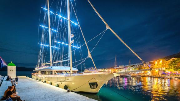 Подсвеченная моторная яхта Son de Mar в порту Сплита ночью, на фоне оживленного города.