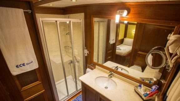 Ece Berrak guletinde geniş bir duş, ayna ve zarif ahşap panellerle donatılmış lüks bir banyo.