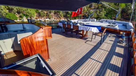 The deck of the gulet 'Ugur' with dining table and seating in front of a green shore backdrop.