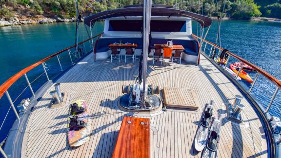 The front deck of the gulet 'Ugur' with dining table, water sports equipment and a quiet bay in the background.