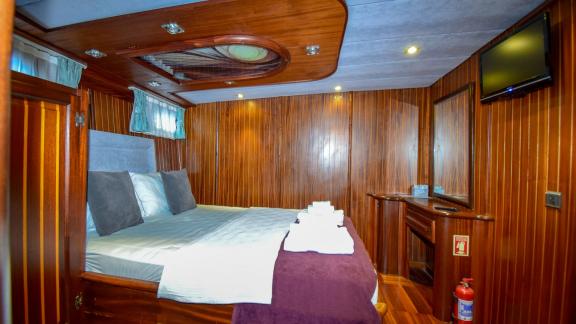 A wood-panelled cabin on the gulet 'Ugur' with a cosy double bed and a television.