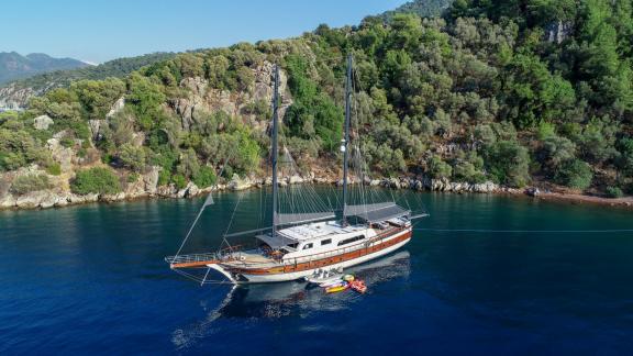 The 7-cabin gulet Ugur 2005 is anchored in the calm waters of Marmaris, Turkey, with a forested coastline in the backgro