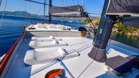 The sun deck of the gulet 'Ugur' with deckchairs and towels in front of a coastal landscape.