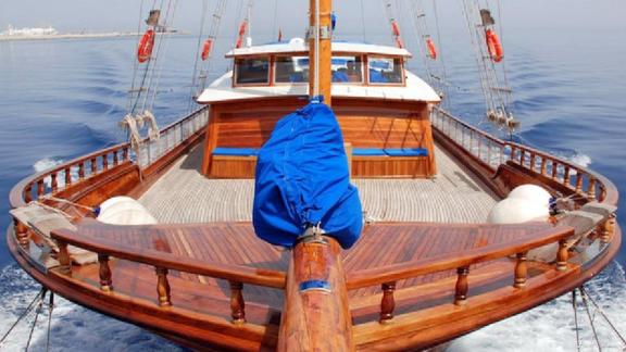 Front deck of the gulet Bahrieli C with wooden interior, blue benches and calm sea in the background.