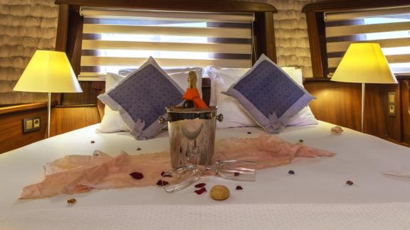 Inviting bed with decorative pillows and champagne in a luxurious cabin of the Gulet Remzi Yılmaz.