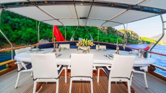 Stylishly laid dining table in the covered outdoor area of the Gulet Remzi Yılmaz with a view of the sea and green hills