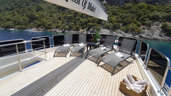 Luxuriöses Sonnendeck der Queen of Makri mit bequemen Liegen und Blick auf die grüne Küste.