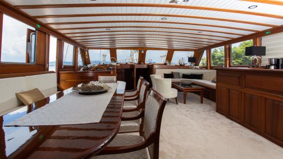 Spacious living room on the upper deck of the gulet, you can see a table with chairs, sofas and a bar