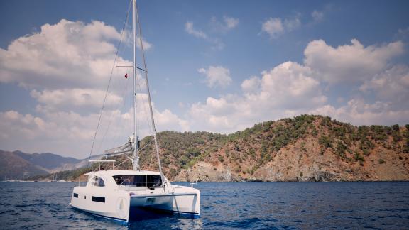 The catamaran Deniz3 anchored in a peaceful bay with mountain views in the background.