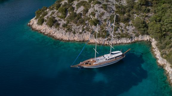 Segelboot in türkisfarbenem Wasser, umgeben von felsiger Küste und grüner Vegetation.