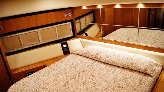 On Noi Quattro in Trogir, a double bed, patterned cover, mirror and warm cabin lights are seen for yacht charter.