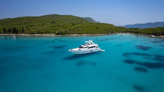 Near Trogir, Sea Side motor yacht rests in a turquoise bay by green hills for a weekly yacht charter.