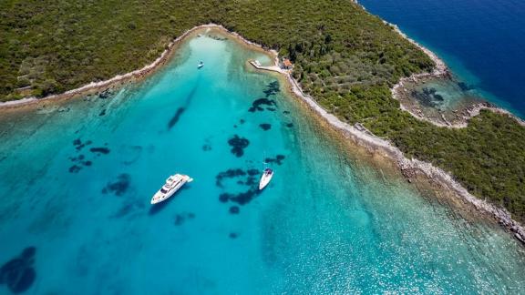 Near Trogir, Sea Side is seen in a turquoise bay with green island shore and boats for weekly yacht charter.