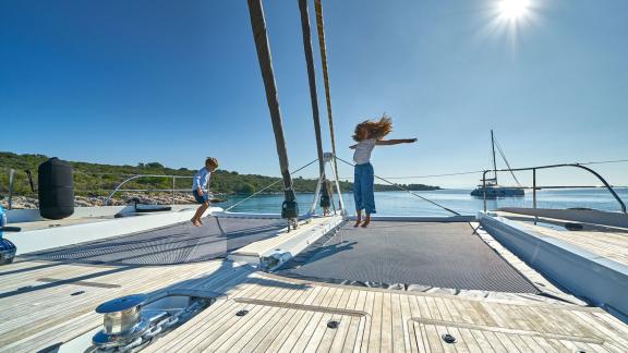 Children enjoying the trampoline on a catamaran's deck under the bright sun.