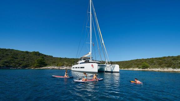 Guests enjoying stand-up paddling and swimming next to the Lagoon Catamaran Adriatic Dragon.