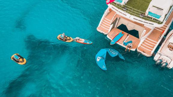 Gäste genießen Wassersportaktivitäten wie Jetski und Paddeln neben dem Katamaran Samara im klaren, blauen Wasser.