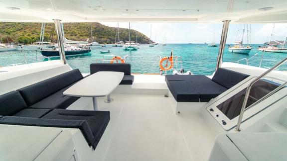 Akana is anchored in a bay with a rear deck featuring sofas and a white table.