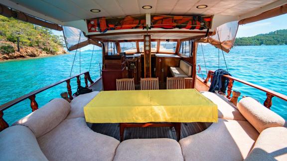 Aft deck of Gulet Lina 2 with a dining table and cozy seating area, surrounded by turquoise water.