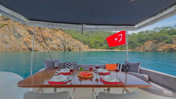 The aft deck of motor yacht Ada Kuzey features a dining area with a stunning view prepared for guests.