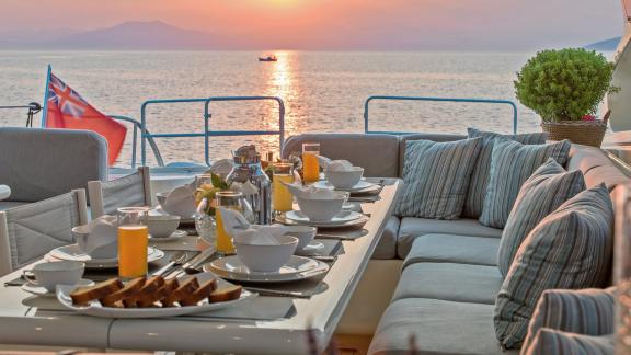 Zu sehen ist das Achterdeck der Atrato in Athen mit gedecktem Tisch bei Sonnenuntergang.