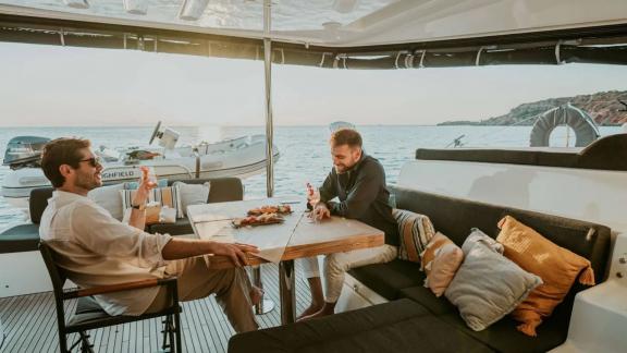 Two friends chatting with snacks on the table on Oneida 2 catamaran.