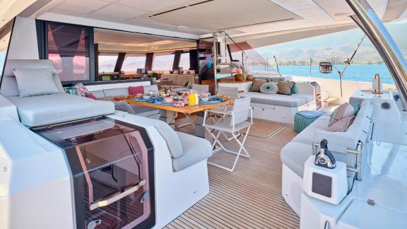 Covered dining area and lounge on the catamaran with a set table and sea view.