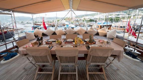 Covered outdoor dining area on the Gulet Optimist with a set table and view of the harbor.