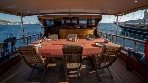 A dining table on the covered deck of a traditional Turkish gulet, prepared for a meal with a view of the sea and Bodrum