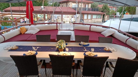 Gedeckter Esstisch und gemütliche Lounge auf dem Deck der Gulet Nirvana 2 im Hafen, mit Hafengebäuden im Hintergrund.