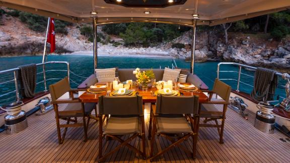 Stylishly set dining area on the deck of a sailing yacht with a view of the coastline.