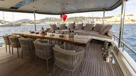 Covered lounge deck of the sailing yacht The Blue Sea with dining table, chairs and seating area.