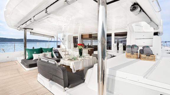 Seating area with cushions, a dining table with flowers, and towels in baskets on the aft of a Lagoon catamaran.