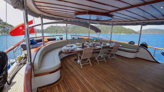 Dining area on the deck of a gulet, with set table and seating, surrounded by seascape and Turkish flag