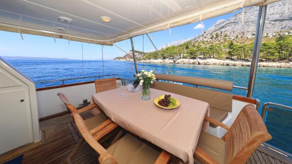 A dining table set on the aft deck of motor yacht Custom Blanka with a view of the scenery.