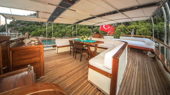 Gemütlicher Sitzbereich auf dem Deck einer Gulet mit türkischer Flagge im Hintergrund.