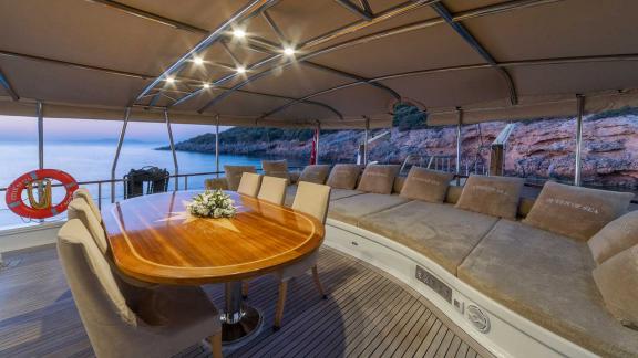 The cosy dining and lounge area on the deck of a Bodrum gulet with 5 cabins, illuminated in the evening hours and set ag