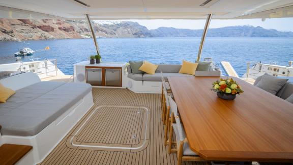 Outdoor lounge with dining area and sea view on a catamaran in a scenic bay.