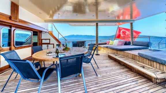 Covered deck with dining table, chairs, loungers, Turkish flag and views of the sea and mountains.