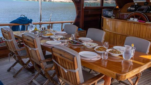 A dining table set on the deck of a traditional Turkish gulet, laden with a variety of dishes.