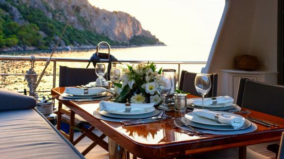 Elegant gedeckter Tisch auf der Segelyacht mit Blick auf das Meer und die Küste im Hintergrund.