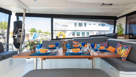 Colorfully set dining table on a catamaran, surrounded by cozy seating and maritime decorations.