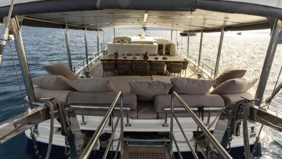 Rear view of the covered lounge deck of the sailing yacht The Blue Sea with seating area and dining table.