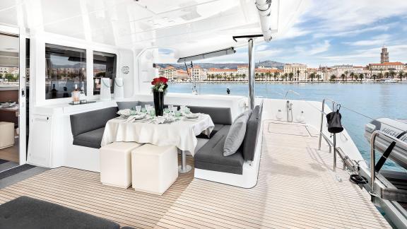 Set dining table with flowers and seating area on a catamaran, overlooking a coastal town.