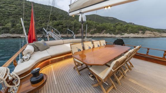 Cosy seating area and dining table on the deck of the gulet yacht Jasemin 1, off the wooded coast.